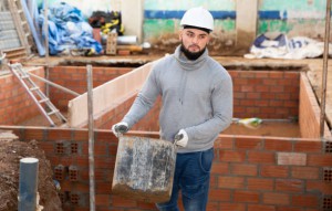 Confident bearded guy working at building site, carrying bucket of construction mortar