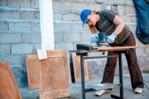 Female Carpenter working with power sander tool on wood cabinet. Woman Restoration and repairing old wood furniture. DIY Crafting at home