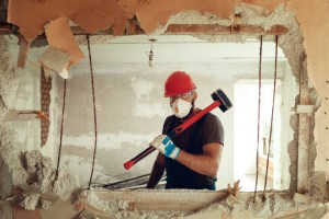 builder with a hammer in his hands breaks the cement wall The builder is dressed in a protective suit and helmet